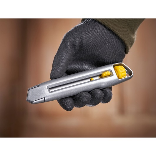 STANLEY 0-10-018 utility knife with yellow slider, held in a gloved hand, side angle view.
