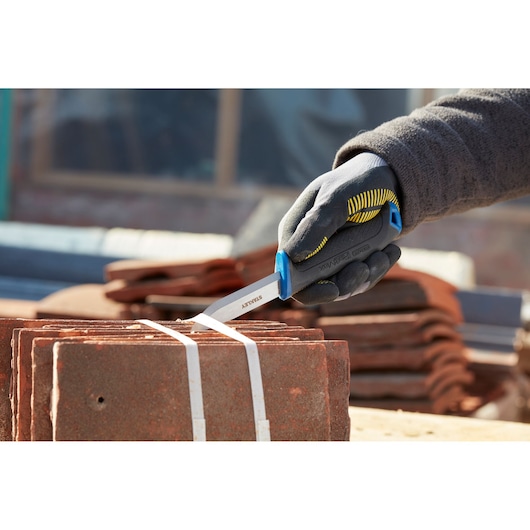STANLEY 0-10-232 folding knife cutting plastic strapping on stacked tiles, handheld close-up.