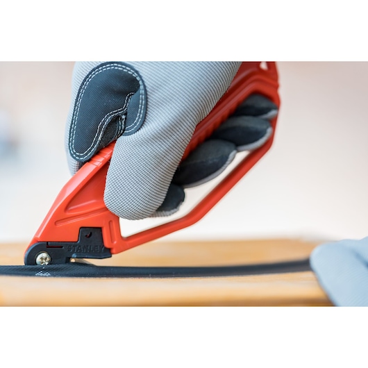 Photo of STANLEY 0-10-244 safety knife with red handle in use, close-up cutting a black material.