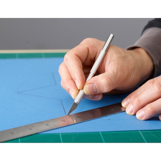 STANLEY 0-10-401 craft knife cutting blue paper along metal ruler, close-up photography.