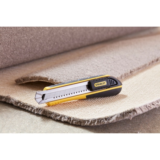 Photo of STANLEY 0-10-481 utility knife with yellow and black body on cut carpet piece.