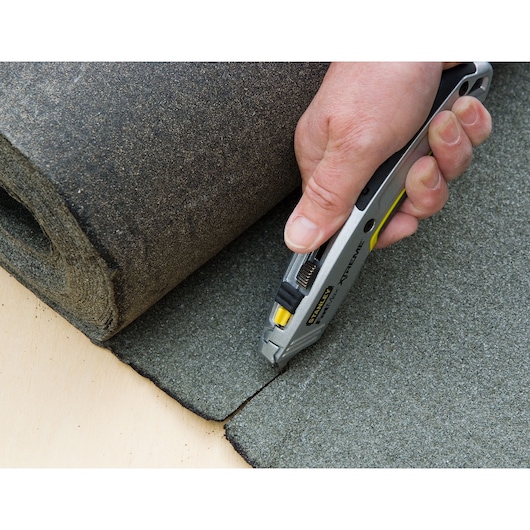STANLEY 0-10-789 utility knife cutting grey roofing material, close-up photo of product in use.