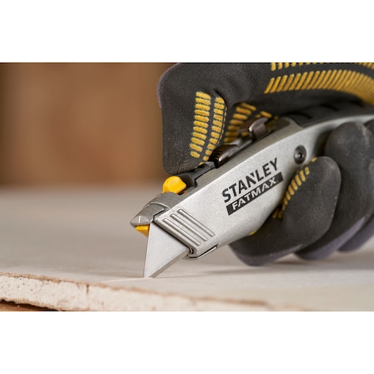 Stanley 0-10-789 utility knife in use, cutting drywall, close-up photo with gloved hand.