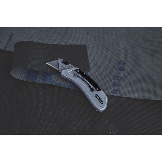 STANLEY 0-10-810 utility knife cutting black fabric, side angle photo.