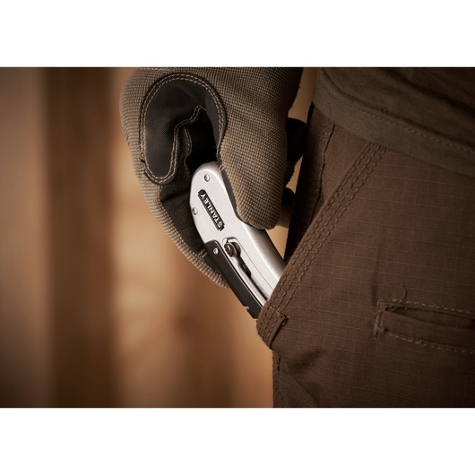 STANLEY 0-10-810 folding utility knife held by gloved hand, being placed in brown pants pocket, close-up.