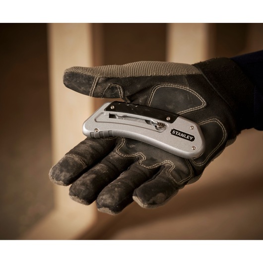 STANLEY 0-10-810 folding utility knife held in a gloved hand, silver with black clip, side view.