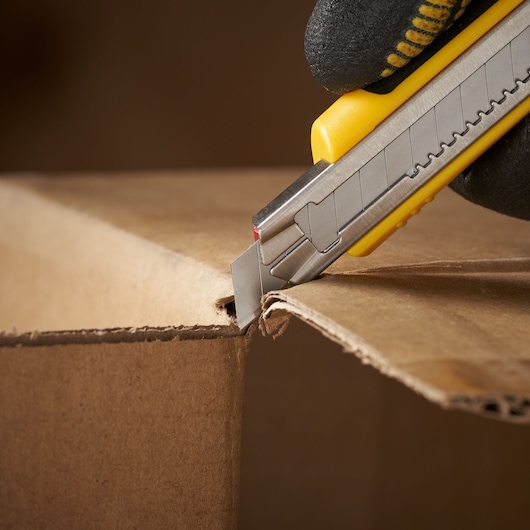 Photo of STANLEY 0-11-300 utility knife cutting cardboard box, close-up side view.
