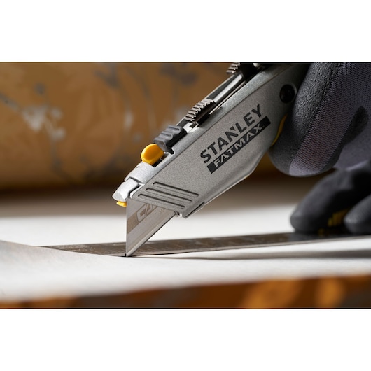 Photo of STANLEY 0-11-800 utility knife cutting material, close-up side angle, hand with glove visible.
