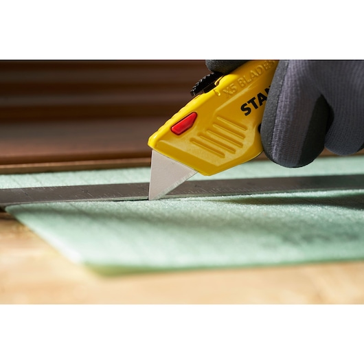 STANLEY 0-11-921 utility knife with yellow handle cutting material along a metal ruler, close-up view.