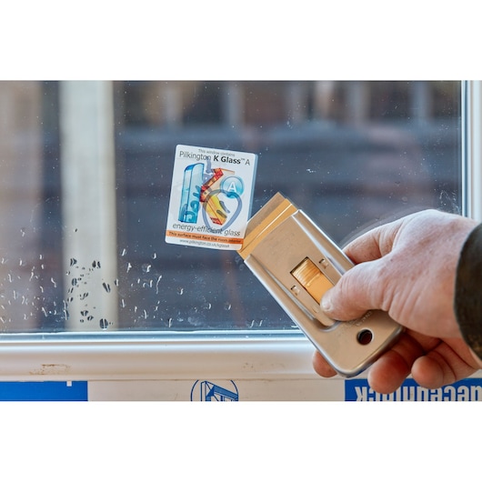 STANLEY 0-28-500 retractable window scraper removing sticker from glass, close-up.