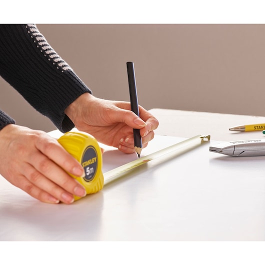 Photo of STANLEY 0-30-497 tape measure in use, close-up angled view, measuring and marking on white surface.