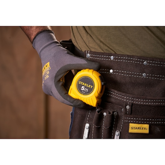 Photo of STANLEY 0-30-497 5m tape measure in gloved hand, clipped to brown tool belt.
