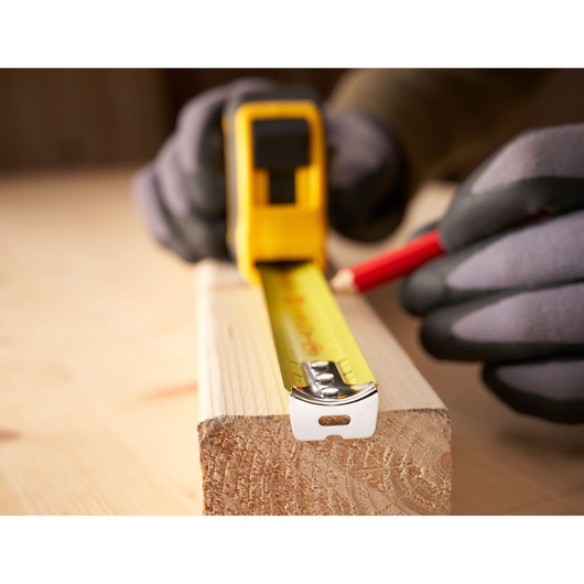Photo of STANLEY 0-30-657 tape measure extended on wood, person marking with pencil, close-up view.