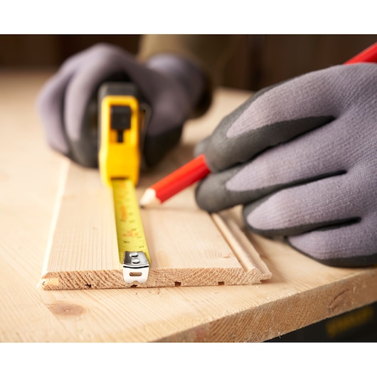 STANLEY 0-30-686 tape measure held with gloved hands, marking wood with pencil, photography close-up.