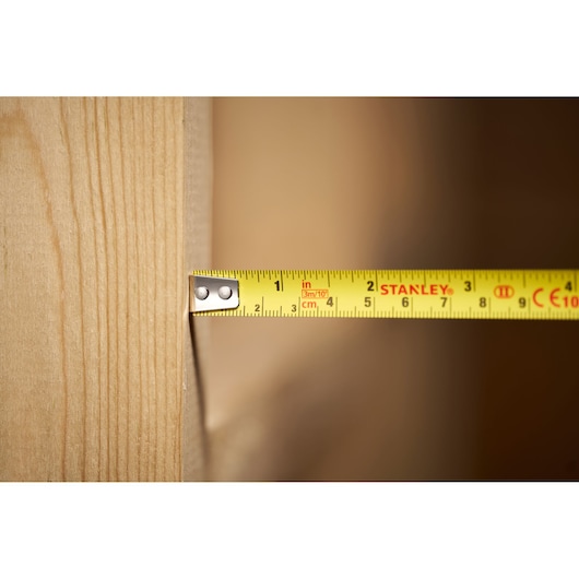 STANLEY 0-30-686 tape measure measuring wood surface, close-up side view.