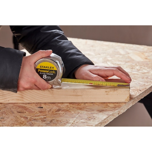 STANLEY 0-33-527 tape measure held measuring wood plank on work table, close-up photography.