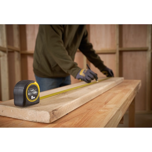 STANLEY 0-33-728 tape measure, yellow and black, on wooden board during woodworking, close-up angle.