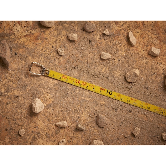 STANLEY 0-34-108 measuring tape extended on dirt with rocks, product photography.