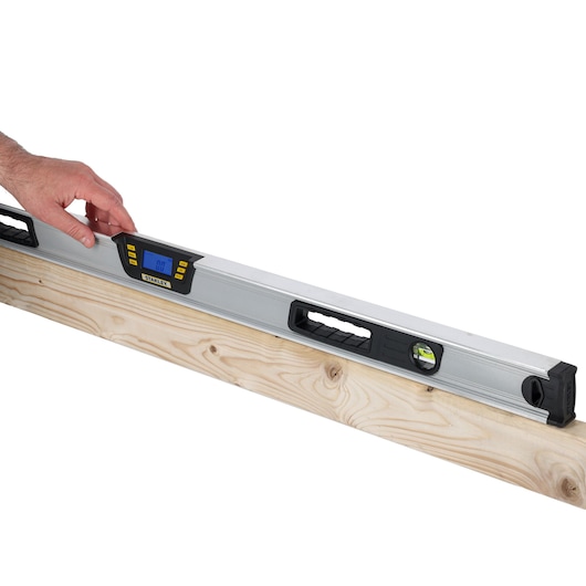 Photo of STANLEY 0-42-086 digital level placed on wood, display screen and handles visible, hand adjusting tool.