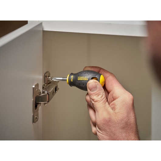 STANLEY 0-65-407 stubby screwdriver with black and yellow handle in use tightening a cabinet hinge.