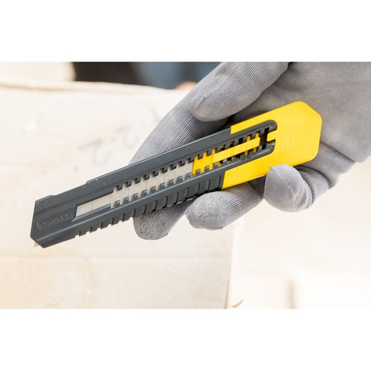 STANLEY 1-10-151 snap-off utility knife, black and yellow, held in gloved hand, close-up photography.