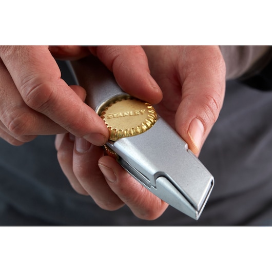 Close-up photo of hands adjusting STANLEY 1-10-550 utility knife with metallic and gold detail.