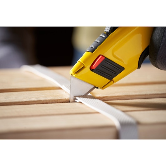 STANLEY 1-11-700 utility knife cutting white strap on wooden surface, close-up side view.