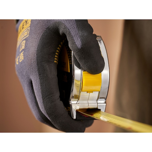Photo of a gloved hand holding a STANLEY 1-33-442 tape measure, yellow and chrome casing, extended measuring tape.