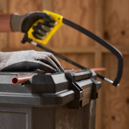 STANLEY 1-70-316 photography of gloved hands using hacksaw to cut copper pipe on black toolbox.