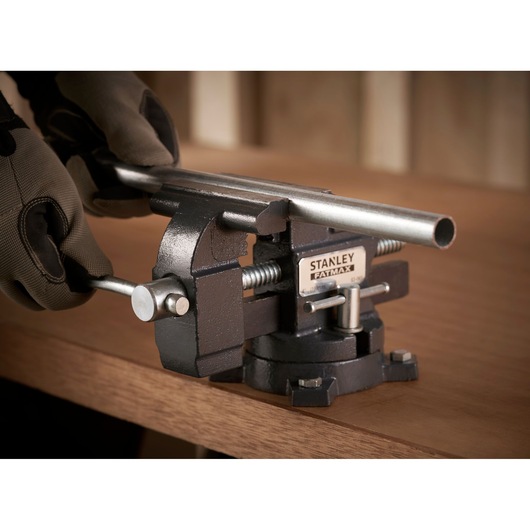 STANLEY 1-83-065 workshop vise clamping metal pipe on wooden bench, close-up side angle.