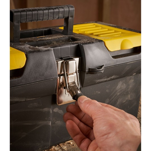 A close-up of a person's hand opening the metal latch on a black and yellow STANLEY toolbox.