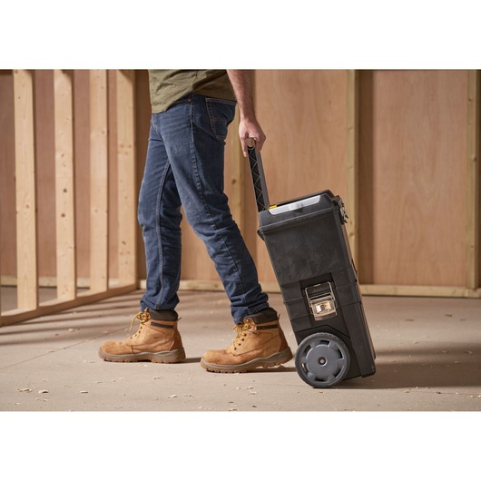 STANLEY 1-93-968 black rolling toolbox with handle, shown being pulled on wheels in a workshop setting.