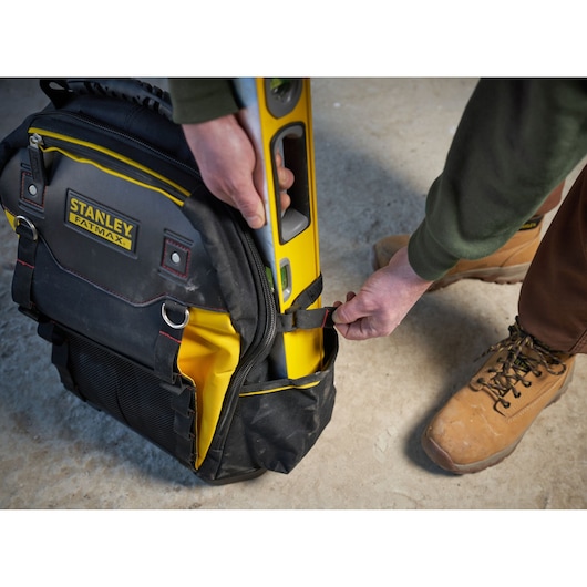 STANLEY 1-95-611 tool backpack holding a yellow spirit level, shown from the side on a concrete floor.