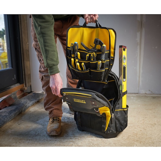 STANLEY 1-95-611 tool backpack with open front, showing organized tools and level, on a workshop floor.