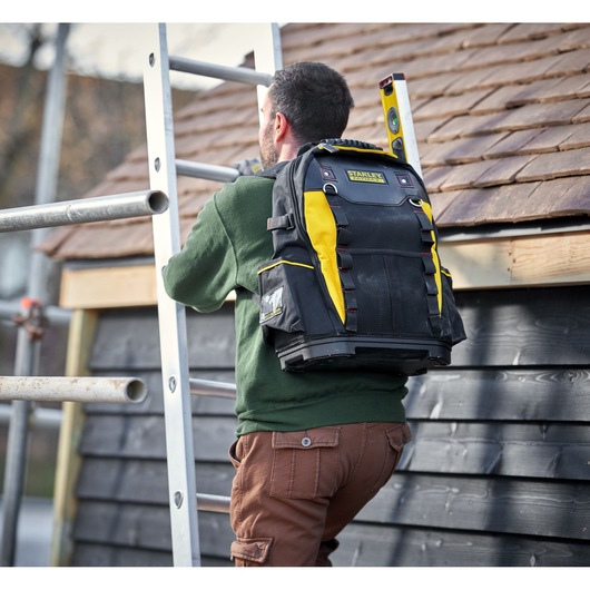 STANLEY 1-95-611 tool backpack in black and yellow shown on a person climbing a ladder outdoors.