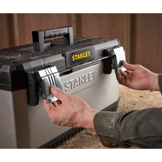 A person opening the metal latches of a STANLEY toolbox in a workshop.
