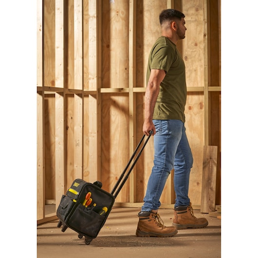 STANLEY 1-97-515 rolling tool bag with tools, carried by person in work boots at construction site.