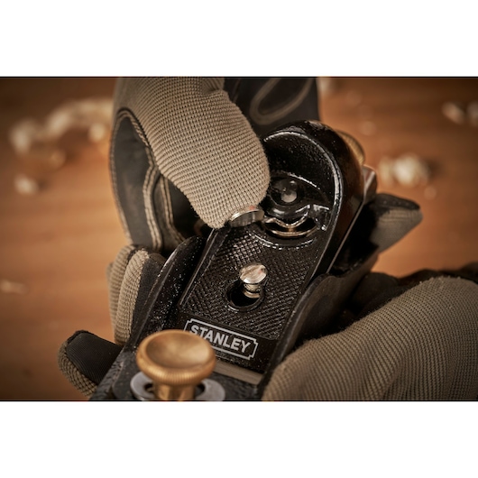 Stanley 12-020 hand plane held by gloved hands, close-up showing adjustment knob on woodworking tool.
