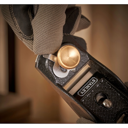 Photo of STANLEY 12-020 hand planer close-up, gold adjustment knob and textured black body, gloved hand holding tool.