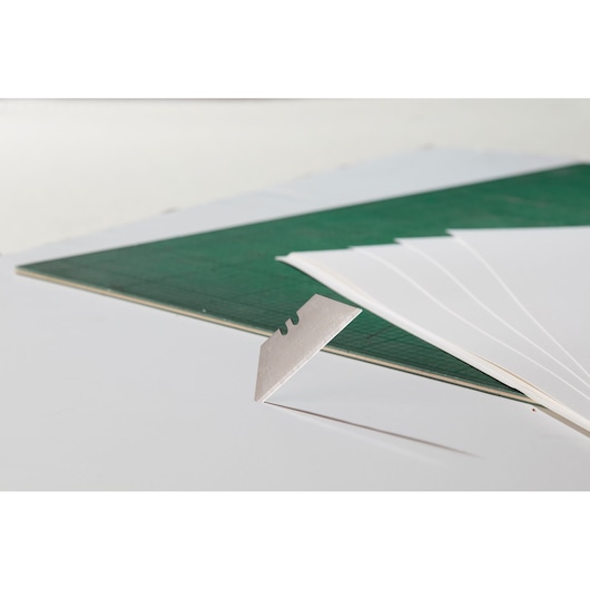 STANLEY 2-11-700 utility blade close-up, beside green cutting mat and white paper sheets.