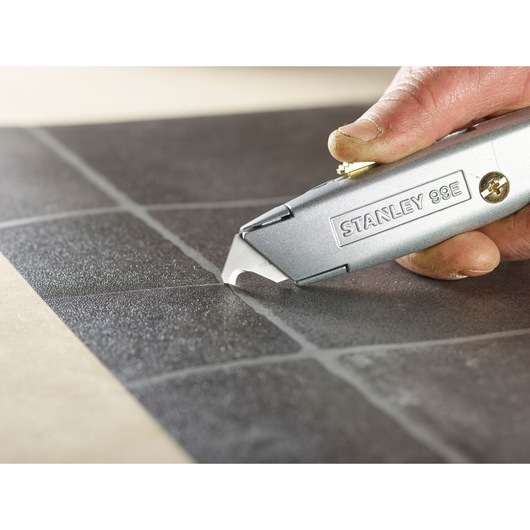 Photo of STANLEY 2-11-983 utility knife scoring black tile, close-up of blade and hand.