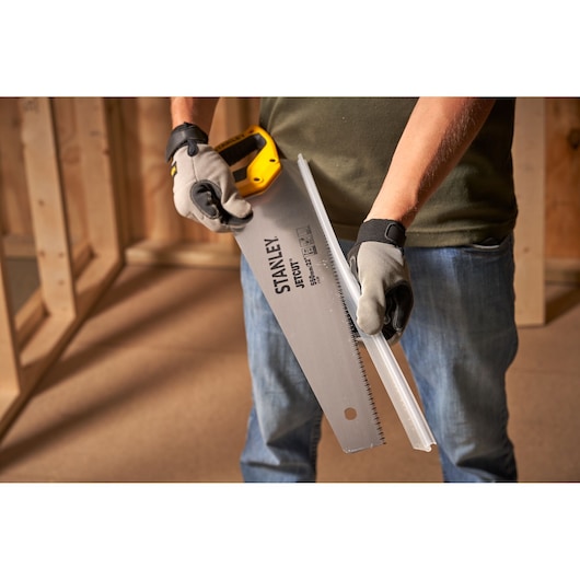 STANLEY 2-15-289 hand saw held by a person with gloves, cutting a plastic strip, indoor setting.