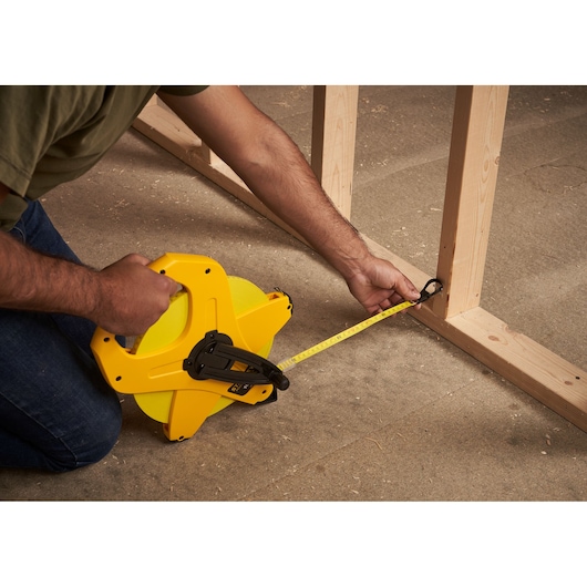 STANLEY 2-34-777 tape measure in use measuring wood framing, side angle, yellow casing.