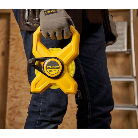 Photo of STANLEY 2-34-792 yellow 30m open reel tape measure held by a worker in gloves, construction setting.