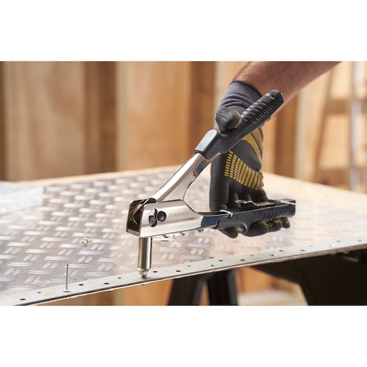 Photo of STANLEY 6-MR55 hand riveter tool being used on a metal sheet in a workshop.