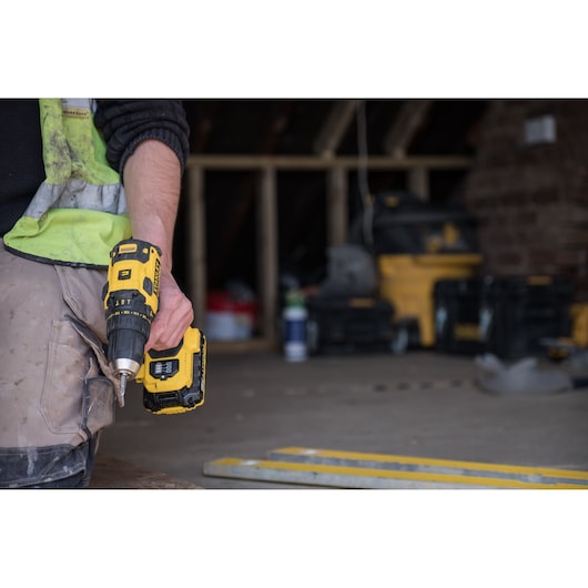 STANLEY FMC627D2 cordless drill held by worker in construction setting, yellow and black, side view.