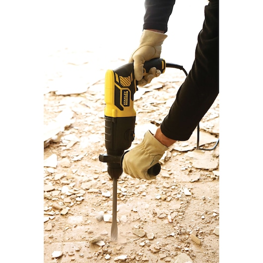 STANLEY FME500K demolition hammer in use on debris-covered floor, worker wearing gloves.