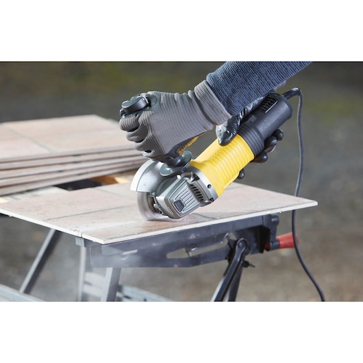 Photo of STANLEY FMEG220 angle grinder cutting tile, product in use on a workbench.
