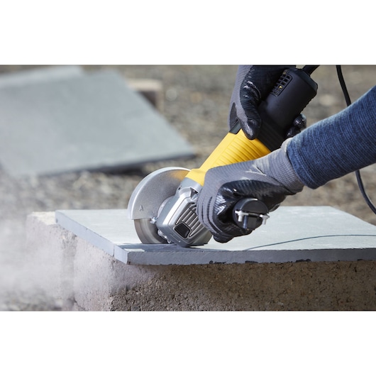 STANLEY FMEG220 angle grinder cutting stone slab, close-up with gloved hands operating.