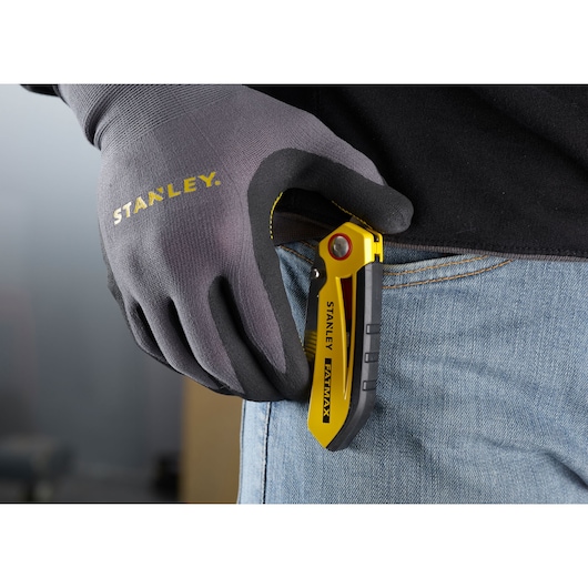 STANLEY FMHT0-10827 folding utility knife in yellow and black clipped to jeans, gloved hand holding it.